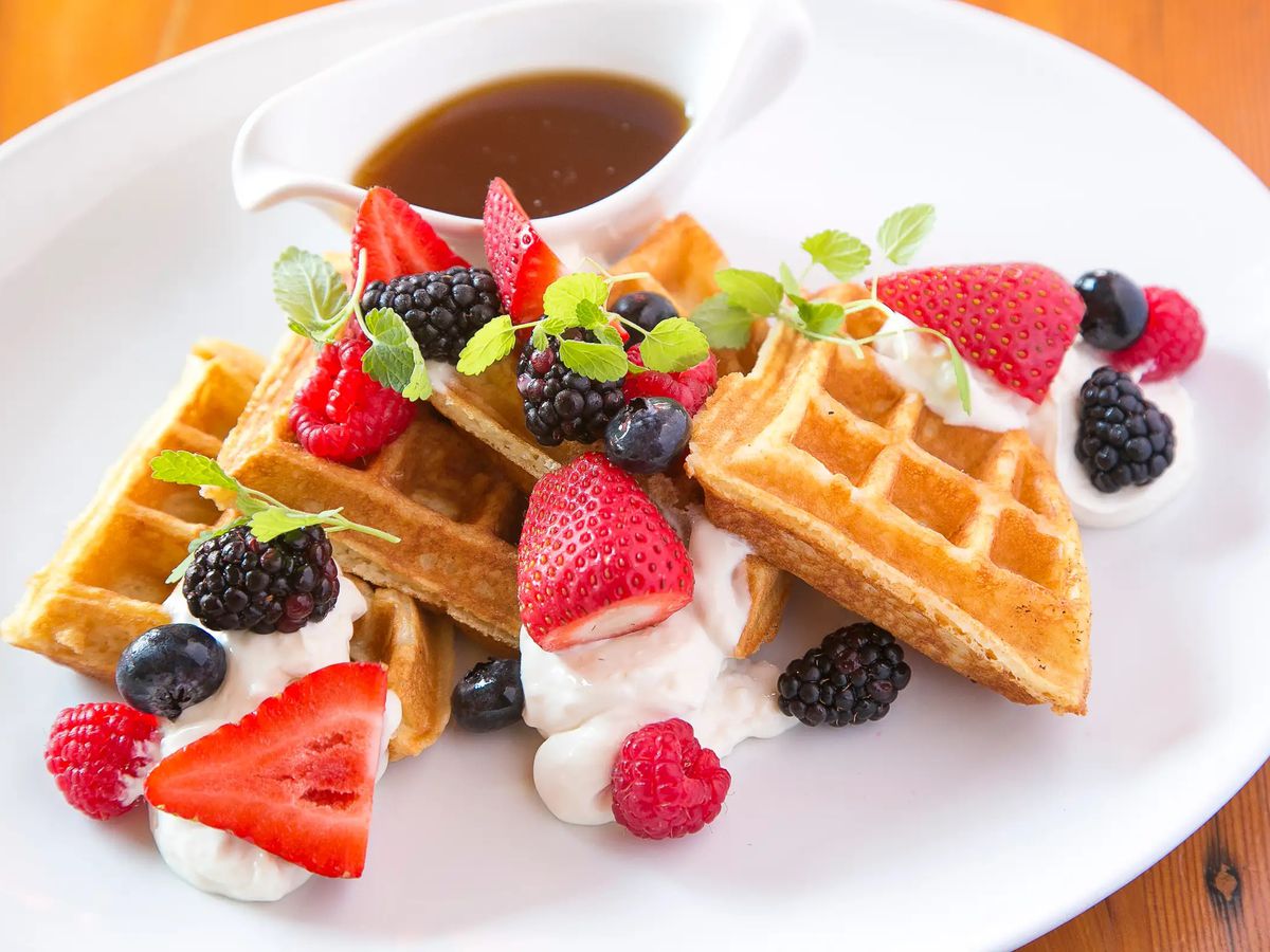 A tilted photo of waffles and strawberries on a white plate.