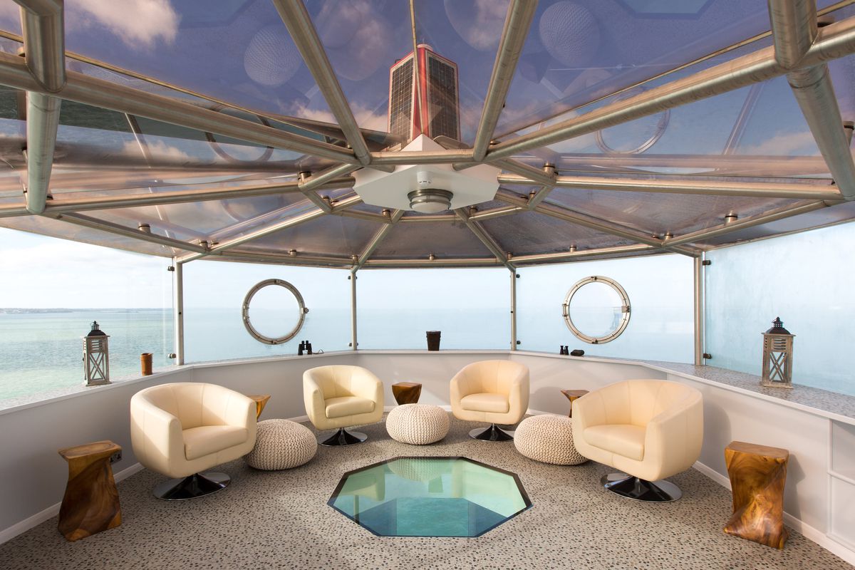 Interior lounge area with views of sea. There are four white arm chairs and windows in a lighthouse style room.