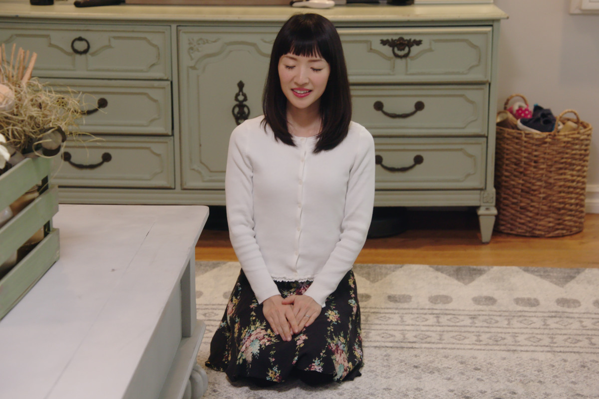 Marie Kondo sitting, with her legs bent under her, in a still from her television show.