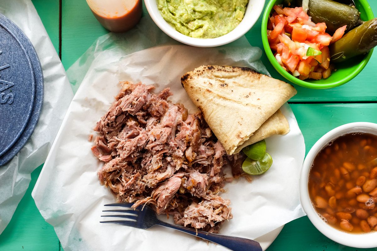 A pile of meat with tortillas and sides.