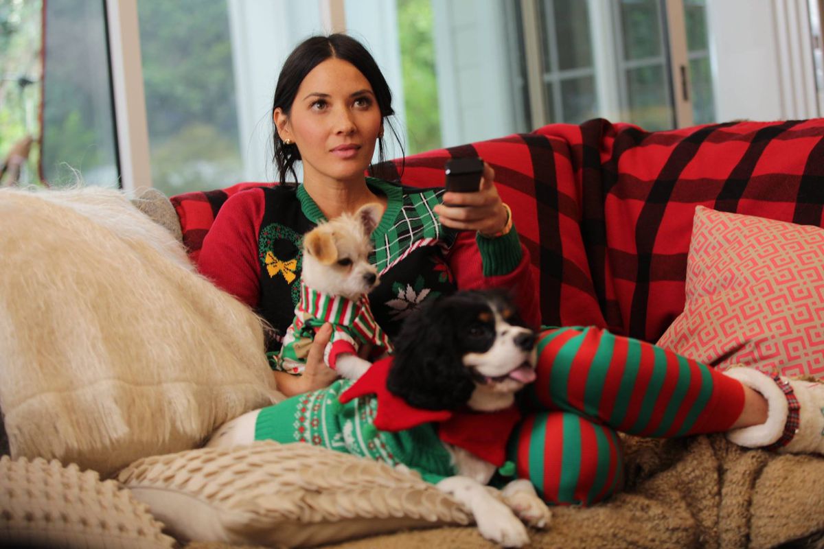 Actress and model Olivia Munn sits on the couch with her two dogs in pajamas. 