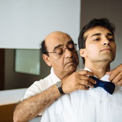 Akash's dad helps him with his tie.