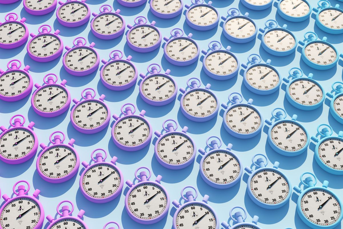 Dozens of purple and blue old-school stop watches lay flat on a blue background.