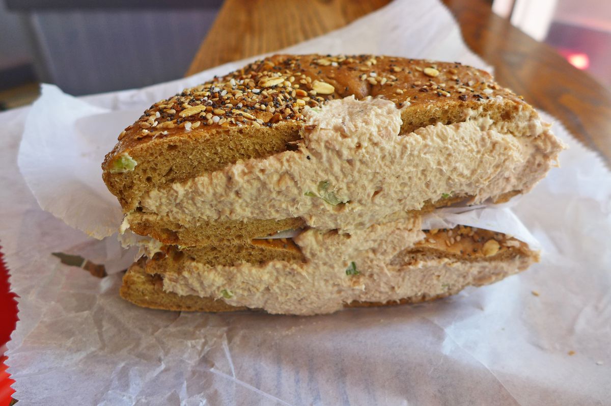 A flattened bagel in the everything format with tuna salad.