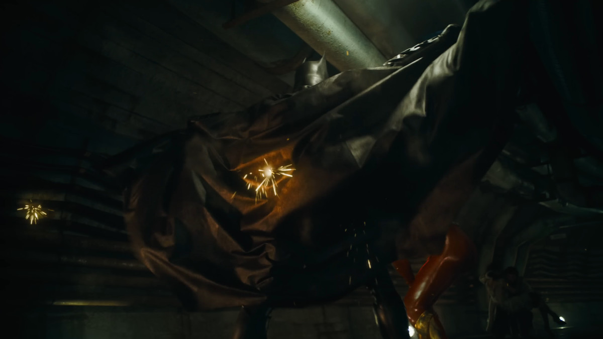 Batman spreads his cape, bullets spark as the ricochet off it in The Flash