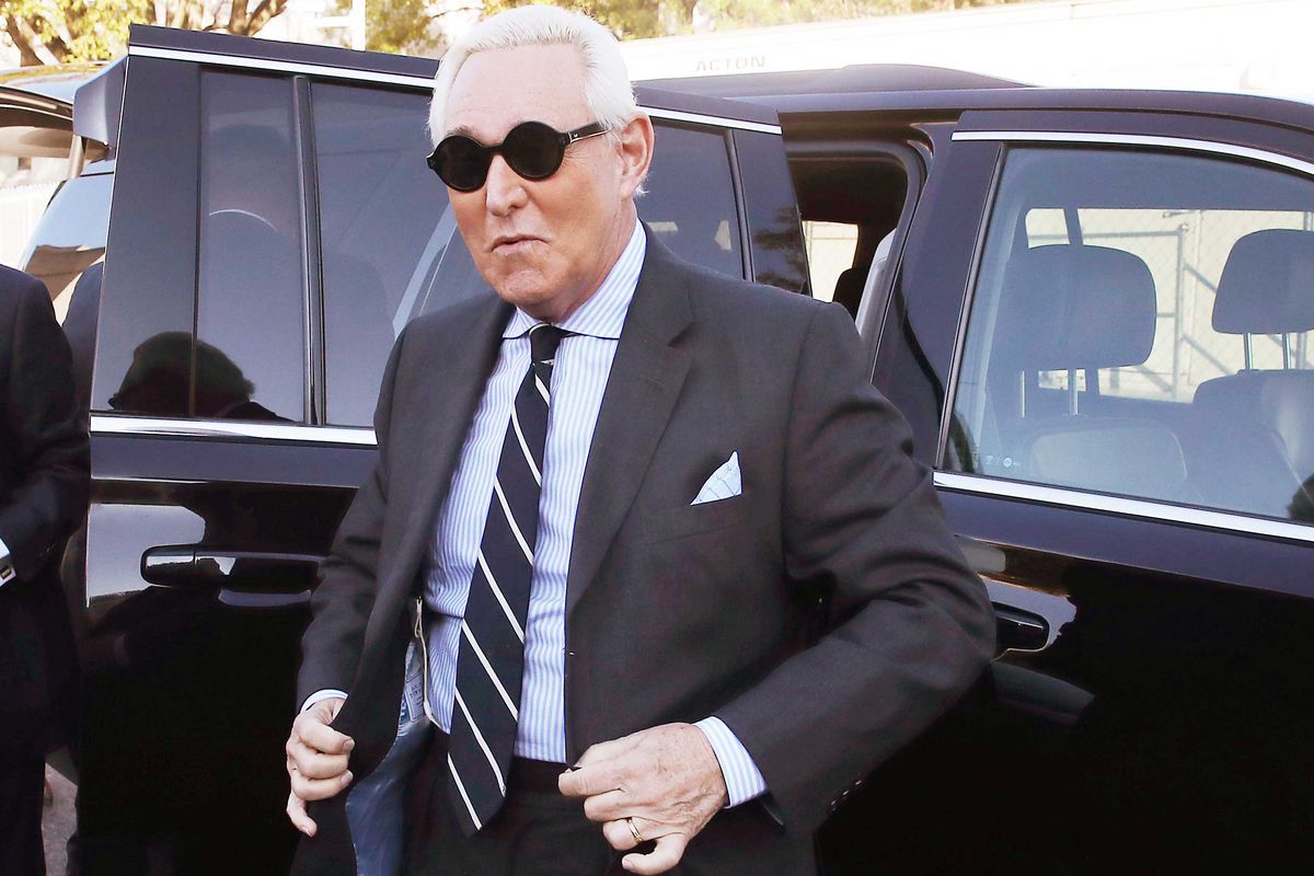 Roger Stone, wearing dark shades and a grey suit, steps out of a car.