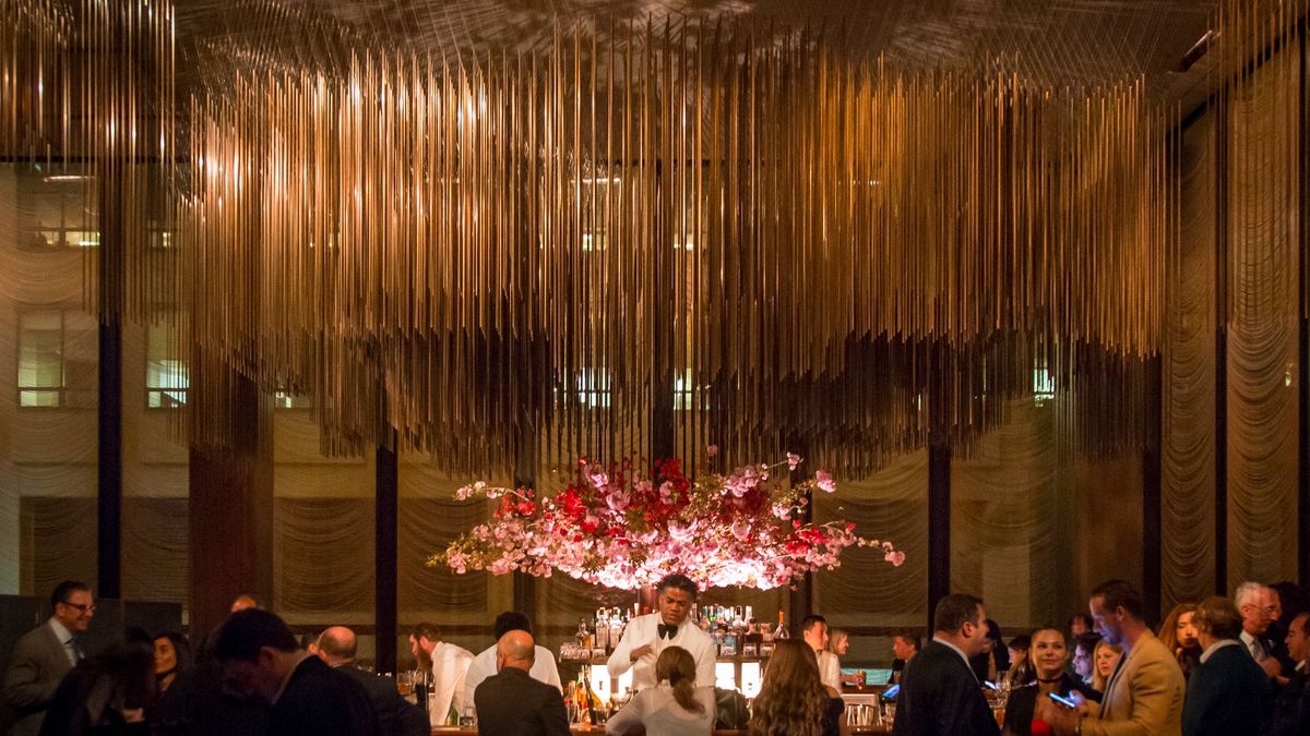 A man in a white tuxedo stands behind the bar at the Grill, in front of a giant arrangement of pink and red flowers