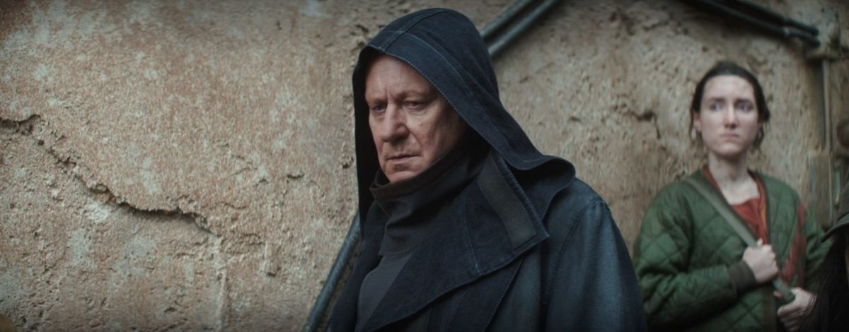 Luther dans un manteau noir avec une capuche se promenant dans Ferrix à Andor
