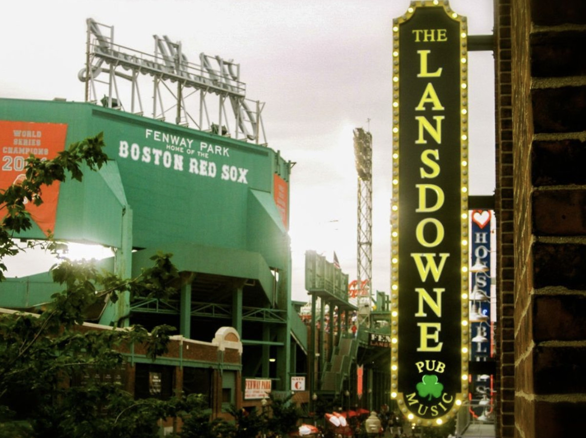 A glittering gold and green sign spelling out the name of the pub, with Fenway Park visible in the background.