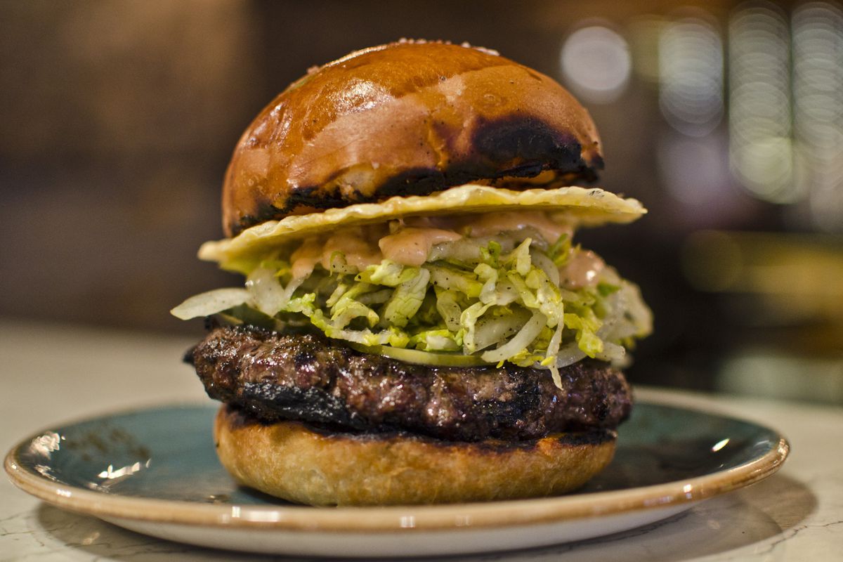 A burger sits on a blue plate, piled high with shredded lettuce, sauce, and a crispy disc of cheese