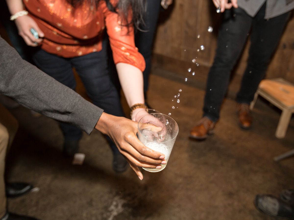 Two people reach out with a glass to catch cider that’s being poured from a barrel