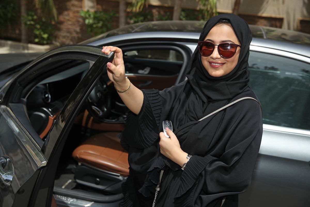 A woman wearing a headscarf stepping into the driver’s seat on a car.