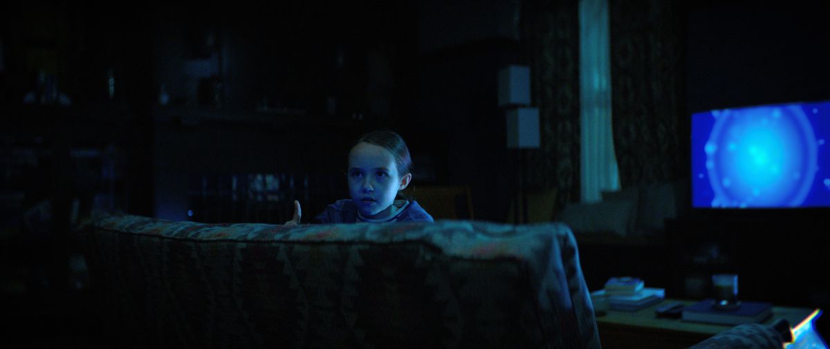Sawyer (Vivien Lyra Blair) peeping over the couch while the blue TV glows behind her in The Boogeyman