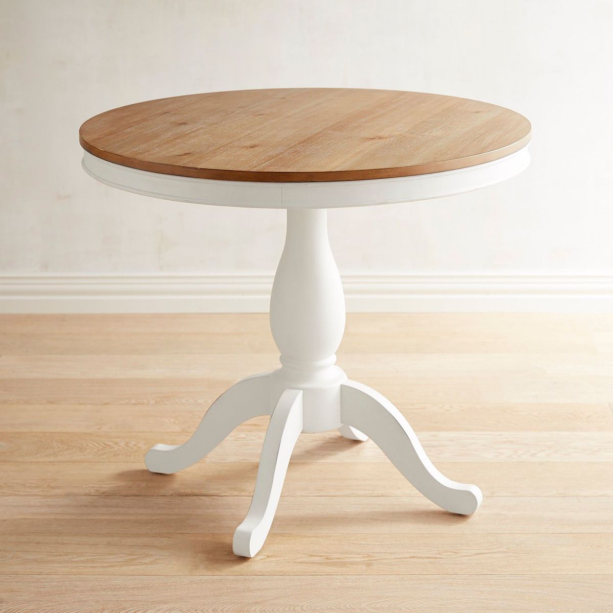 A round table with a natural wood top and white base with four legs. 