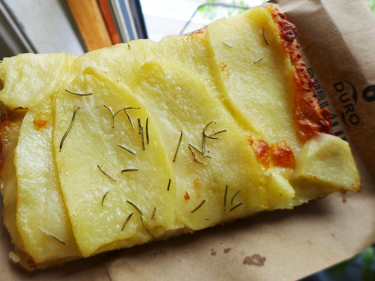 A rectangular slice of pizza with potatoes and rosemary on top.