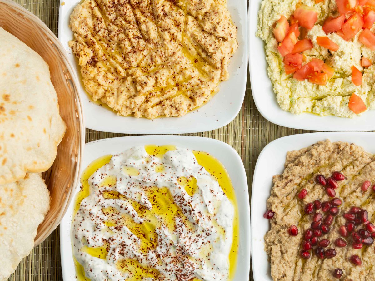 A close-up image of five dishes with hummus and pita bread on them.