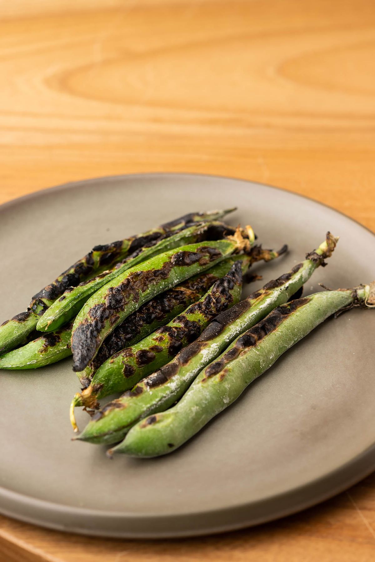 Seared long beans on a slate plate against a wooden table.