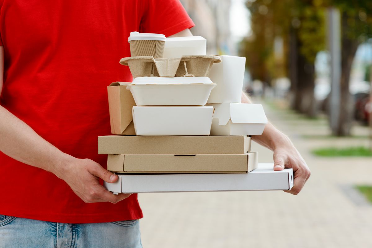 Diverse of paper containers for takeaway food. Delivery man is carrying pizza, Chinese noodles, burgers and coffee. 