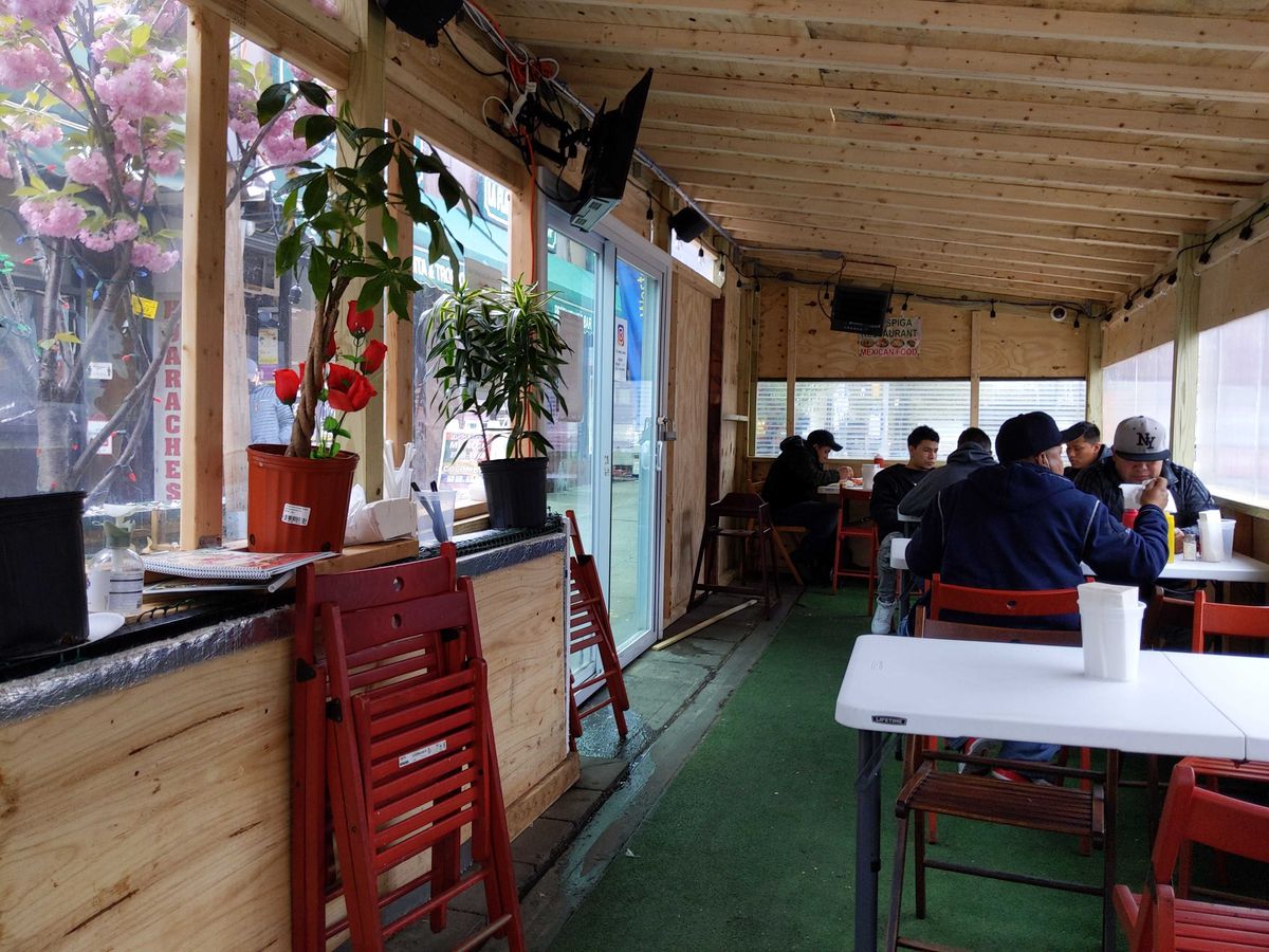 A handful of customers sit at plastic, fold-up tables inside of an enclosed outdoor dining structure