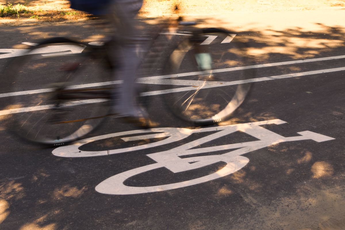 A bicycle is captured in a blur as it speeds over a white bike lane sign on a concrete road.