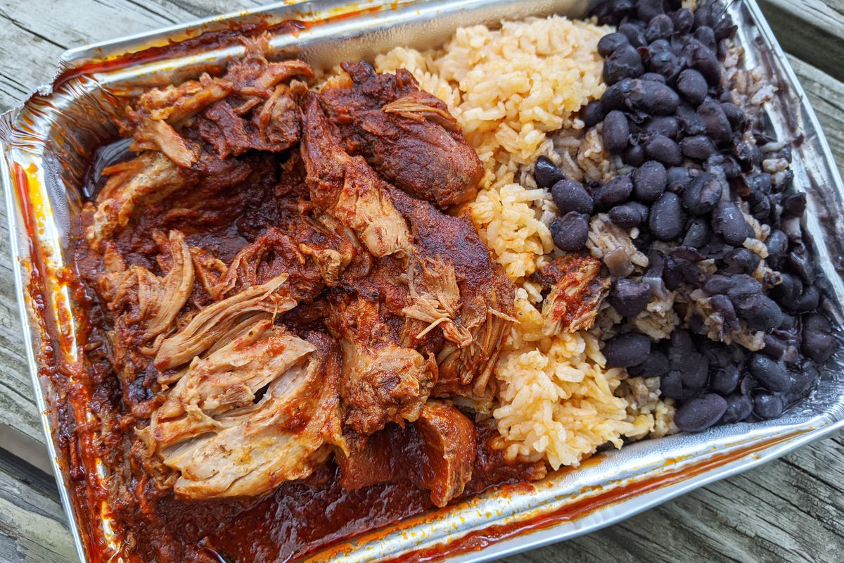 An aluminum vessel with pork in red sauce, black beans, and yellow rice.