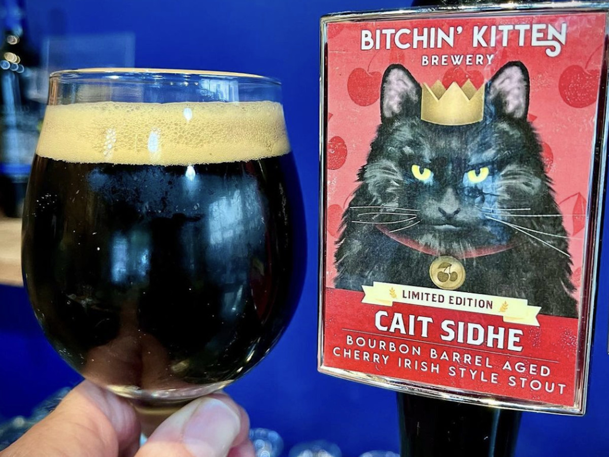 A pint of beer next to a tap with a label that includes a black cat. 