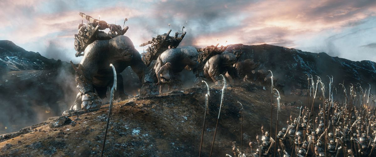 A marching line of troll-mounted siege weapons crest a hill, facing off against another army in The Hobbit: The Battle of Five Armies.