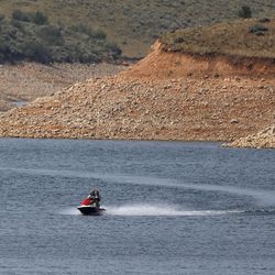 Low water levels are visible as a person rides a personal watercraft on East Canyon Reservoir in Morgan County during a drought in Utah on Wednesday, June 16, 2021.