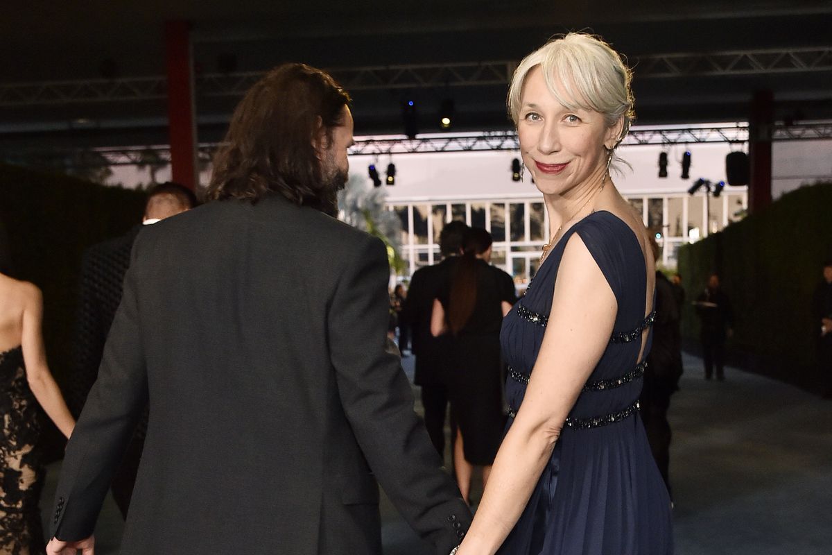 Keanu Reeves and Alexandra Grant hold hands and walk away from the camera; Alexandra looks back over her shoulder.