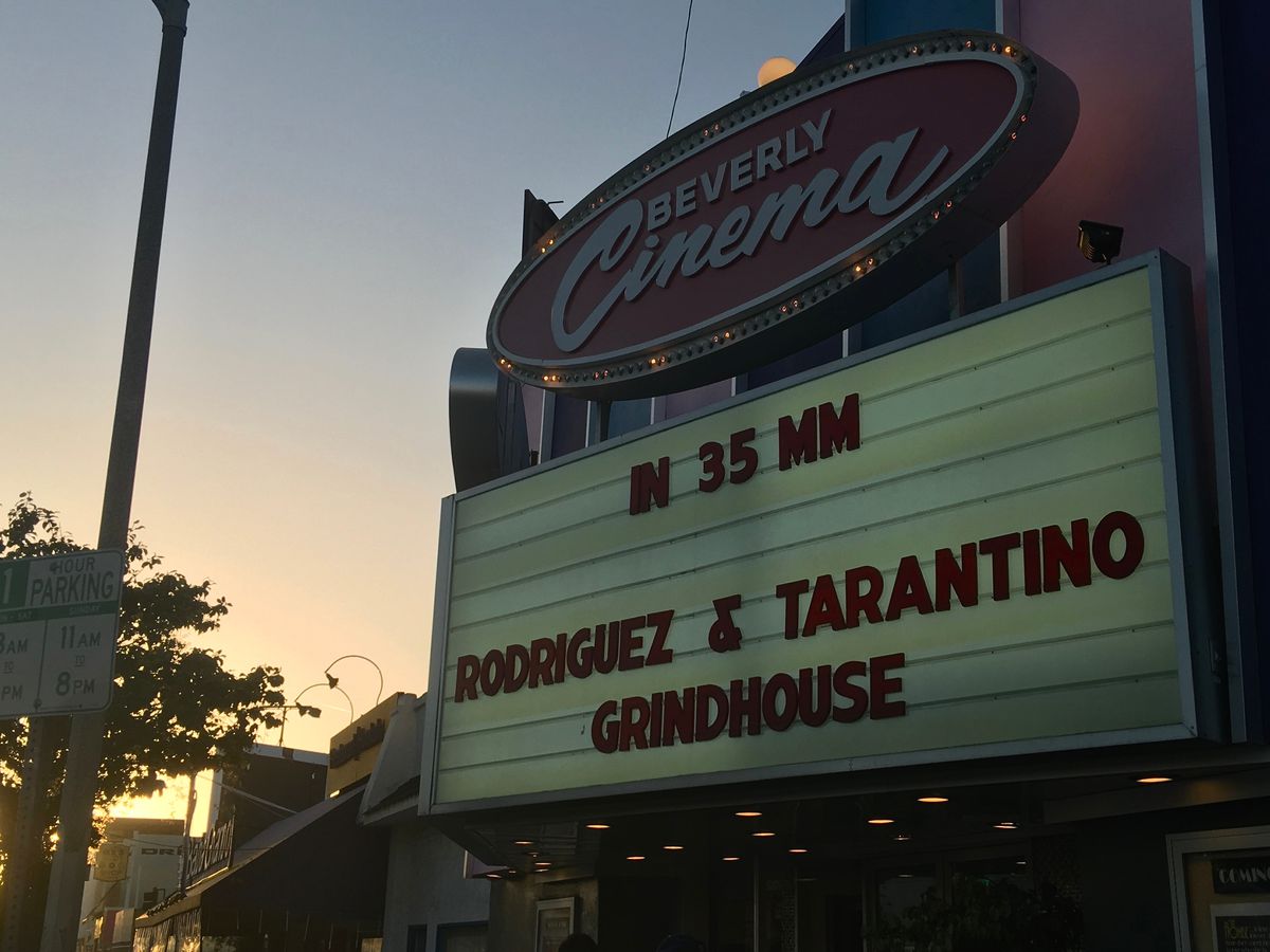 A theater marquee against a sky colored purple and orange in the sunset. The marquee reads “In 35 mm Rodriquez and Tarantino Grindhouse”