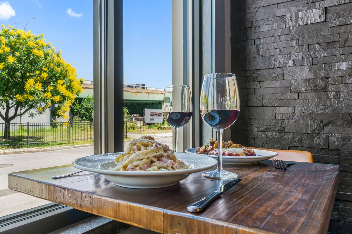 Two plates of carbonara and two glasses of red wine sit atop a high-top table