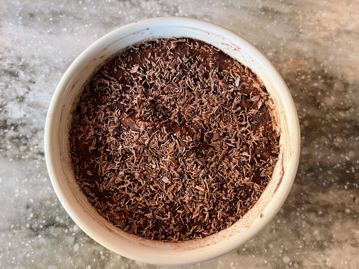 An overhead shot of a bowl of tiramisu topped off with cocoa powder and lots of chocolate shavings.