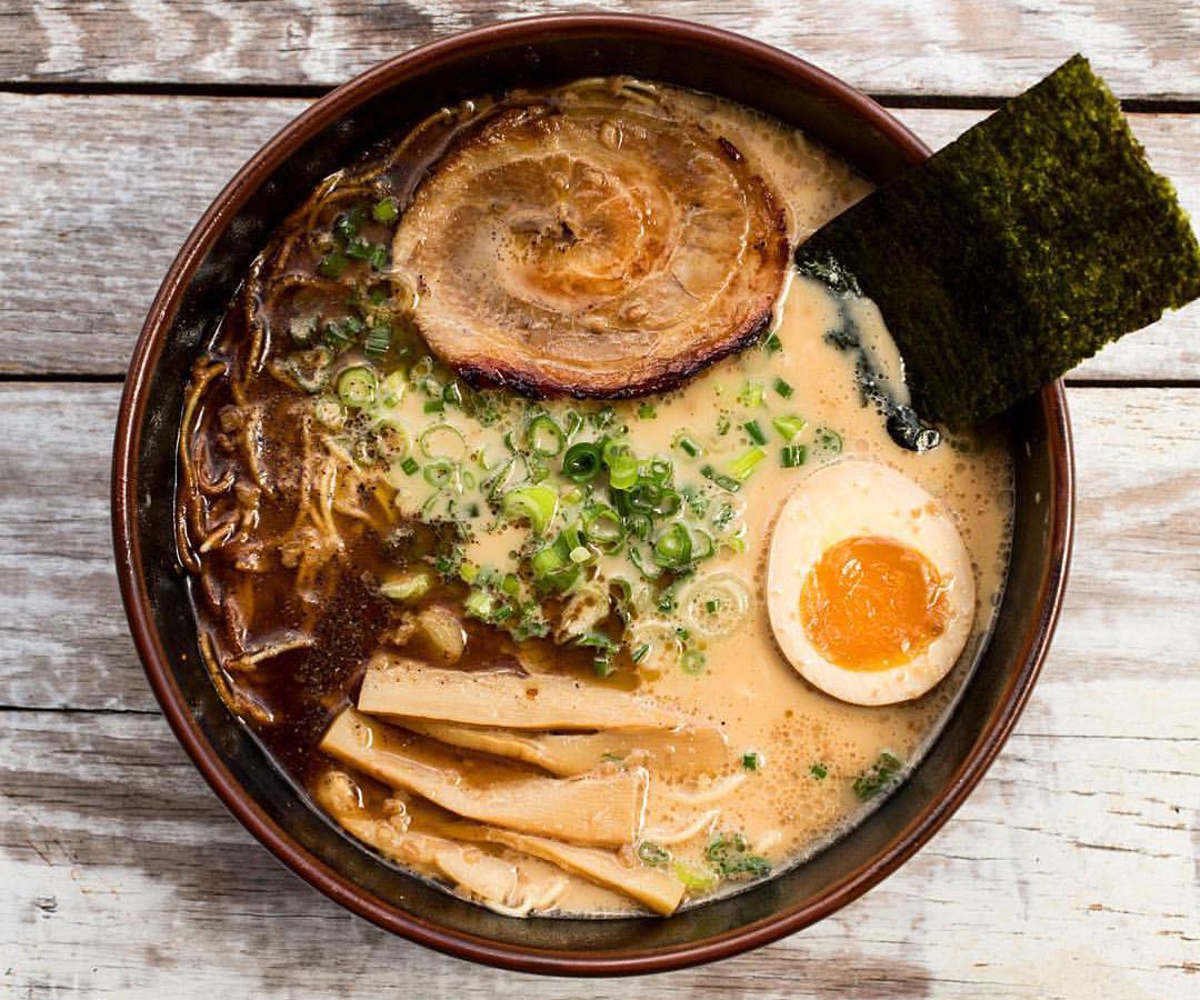 A bowl of ramen with creamy broth, sliced bamboo shoots, half a hard boiled egg, greens, a pork belly slice.
