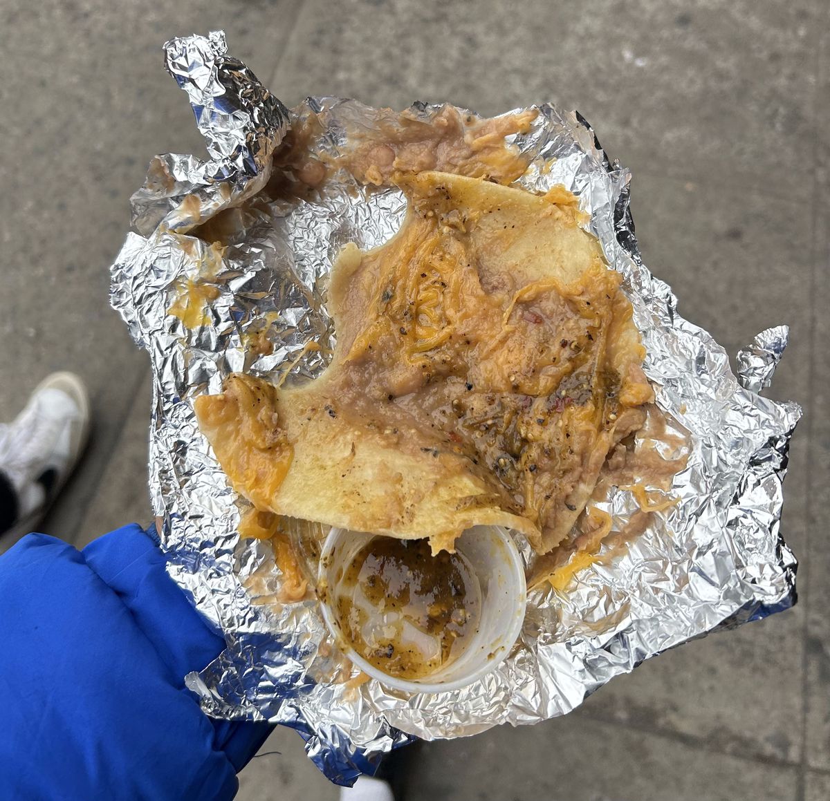 An overhead photograph of a bean and cheese taco in aluminum foil.