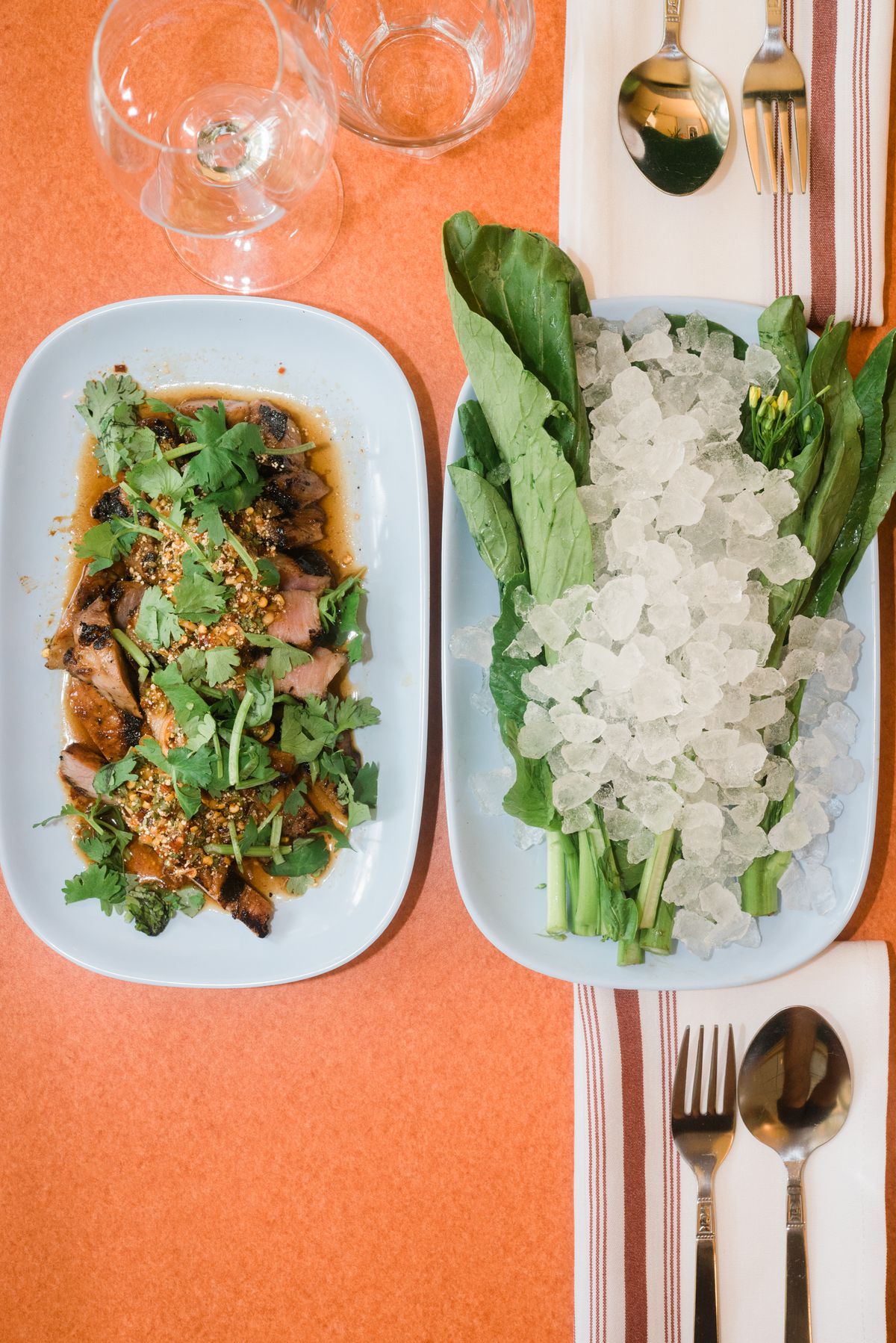 two dishes one with pork and herbs, the other with iced leafy greens on orange tabletop