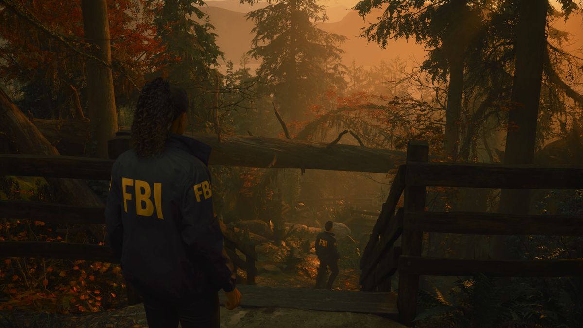 FBI agent Saga Anderson follows her partner Alex Casey down a steep forest path in Alan Wake 2, with a beautiful sunset in the background