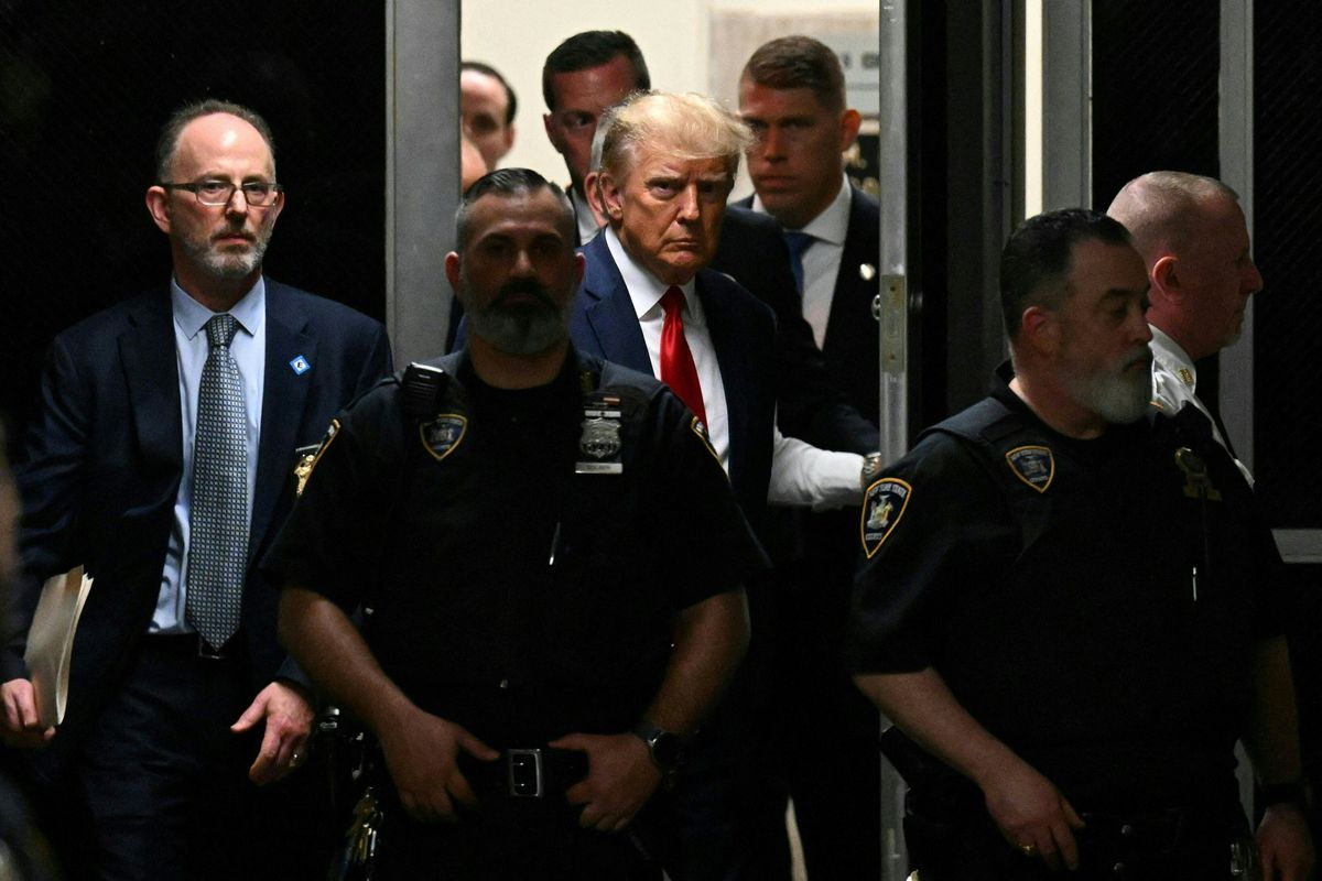Trump enters through a door guarded by police officers.