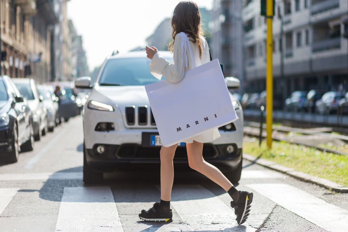 A woman walking across the street holding a Marni shopping bag