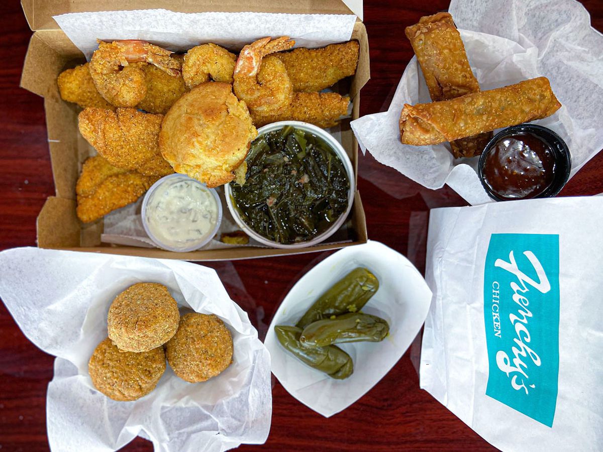 A spread of fried catfish, fried shrimp, jalapeños, egg rolls, hush puppies, greens, and French biscuits.