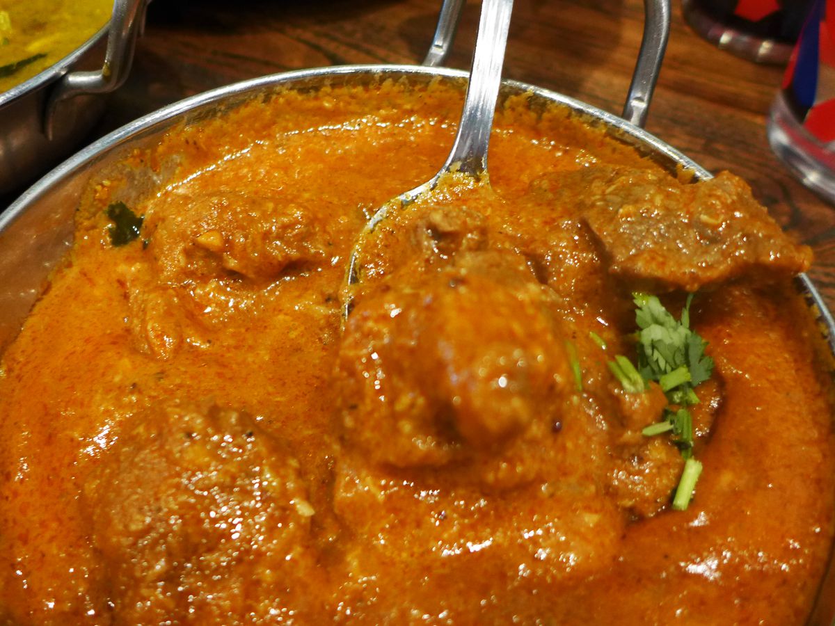 A spoon lifts a bite of reddish brown curry aloft.