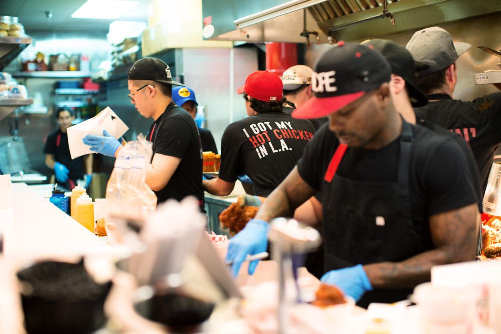A close group of restaurant employees work together inside a small kitchen selling chicken.