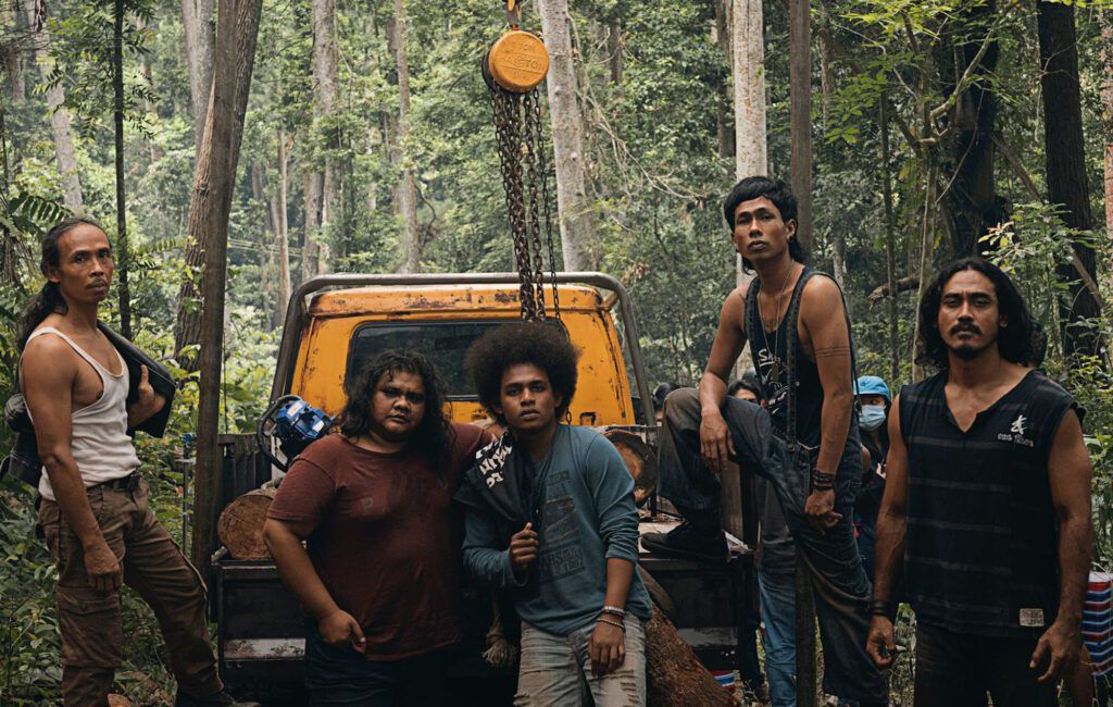 Five people stand behind a pickup truck in the jungle.