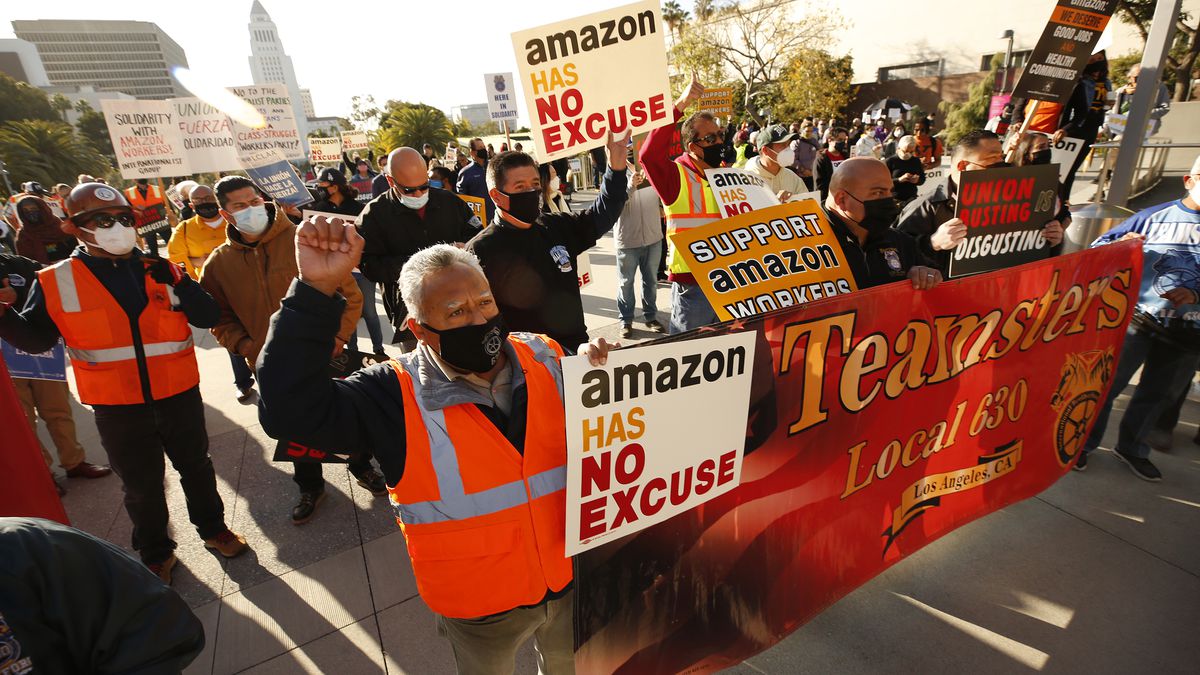 Protesters walking down a city street carry signs that read “Teamsters,” “Support Amazon workers,” and “Amazon has no excuse.”