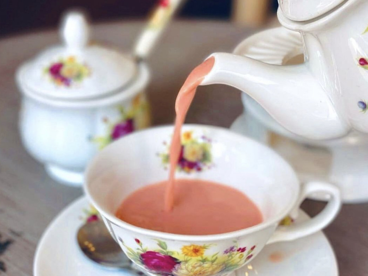 A pink milk tea being poured in a china tea cup. 