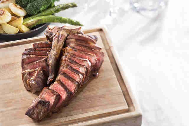 A carved steak on a cutting board, with green vegetables in the background.&nbsp;