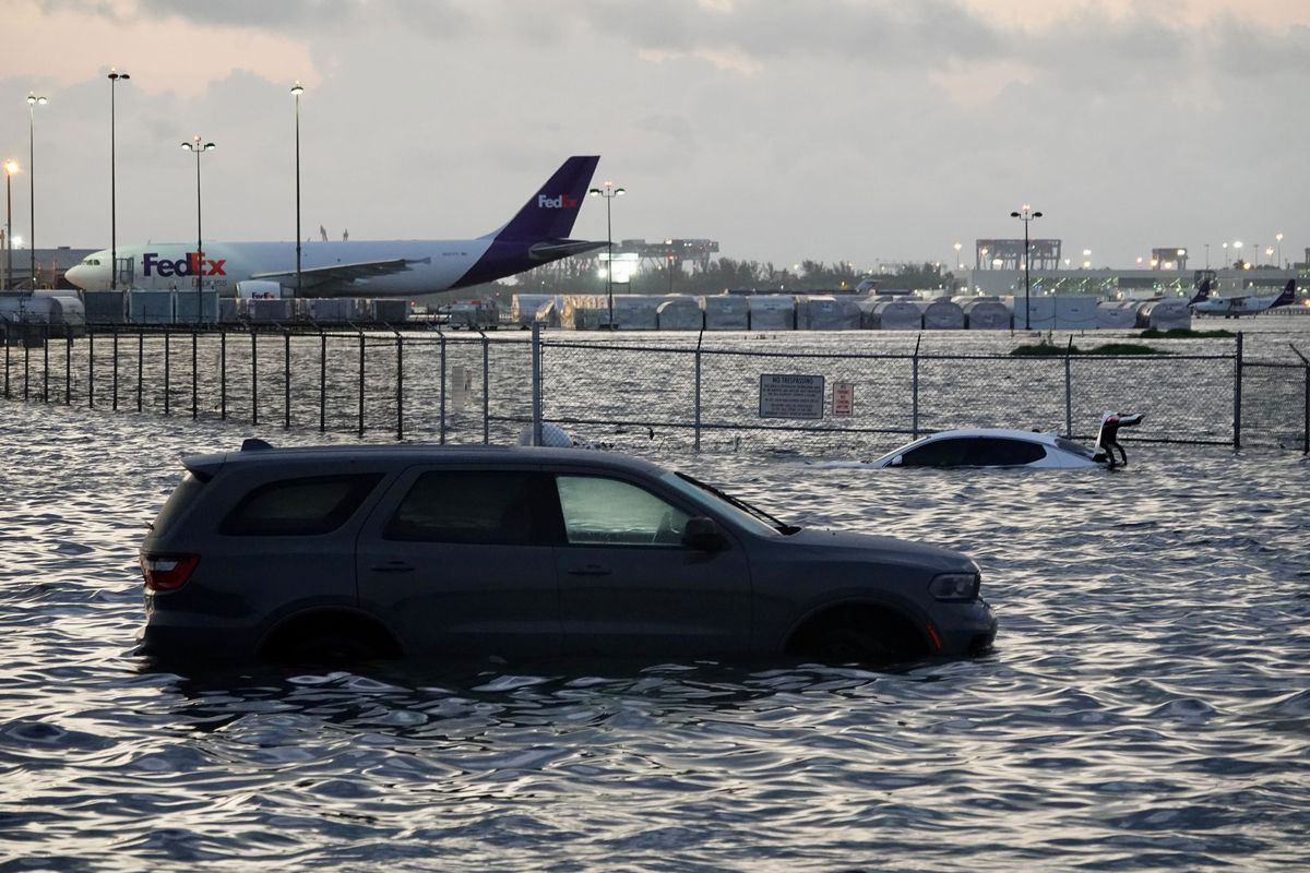A parked SUV in water above its wheels. An airport and planes are in the background.