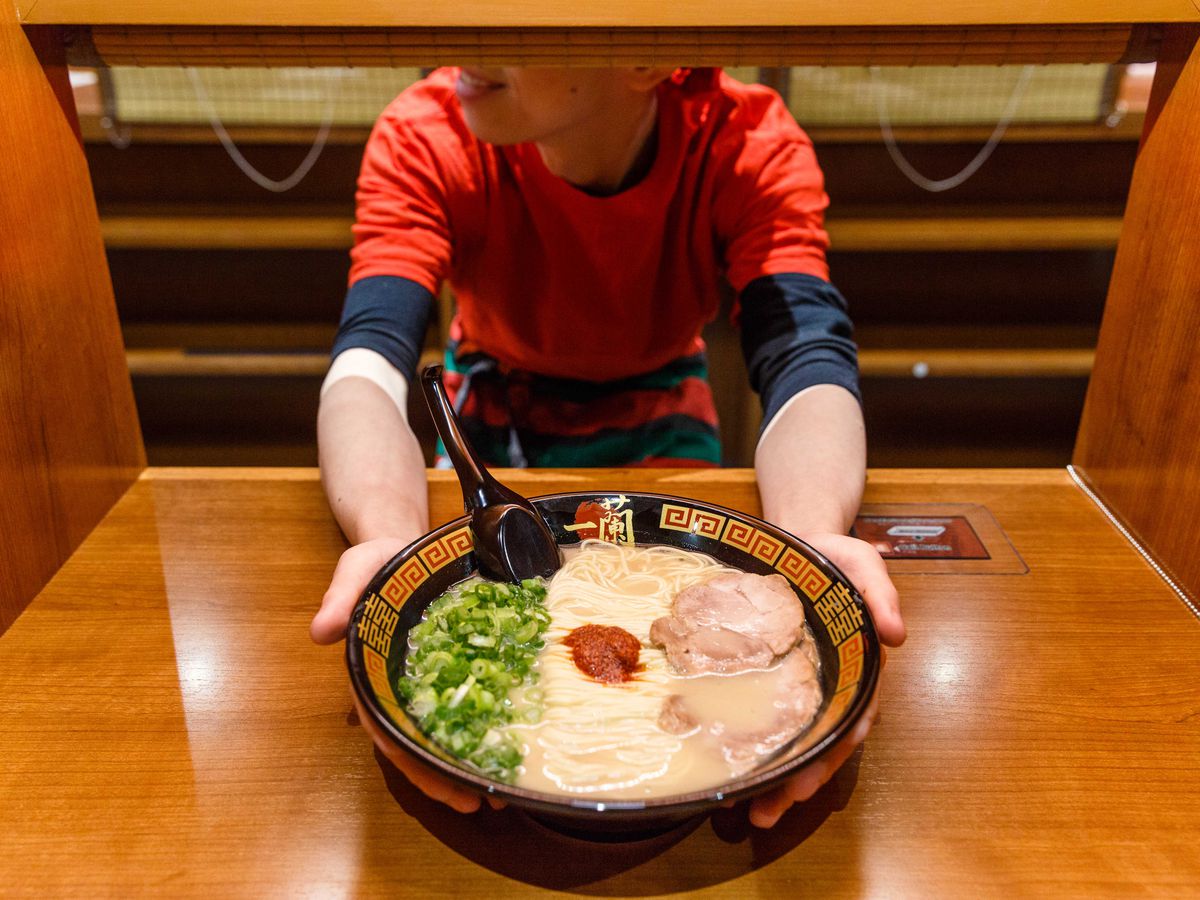 A man hands off a bowl of ramen to the camera.