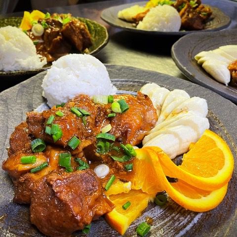Chicken and pork in a sauce topped with chopped scallions, served with orange wedges and rice.  