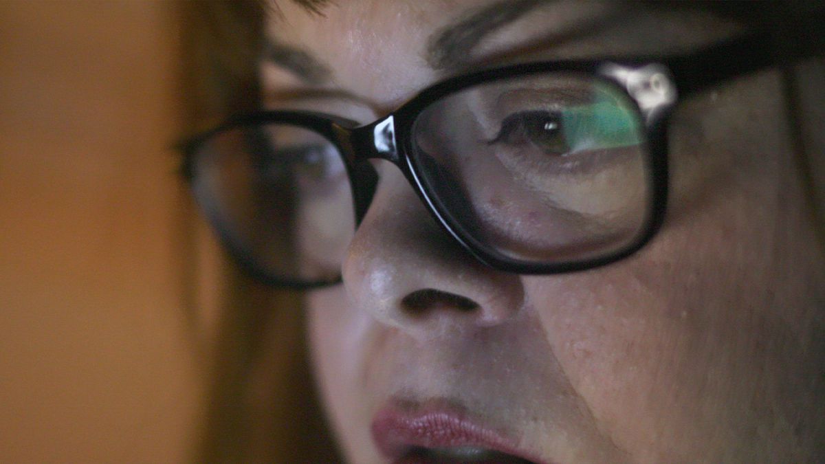 A close up shot of a woman wearing glasses as she stares at a screen.