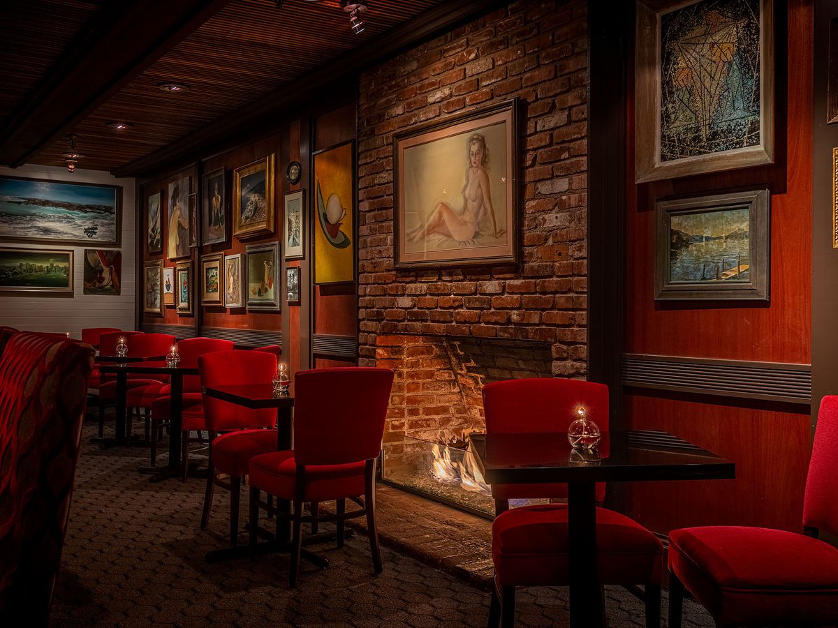 A bar with brick walls, a fireplace, and red chairs at Dear Jane’s.